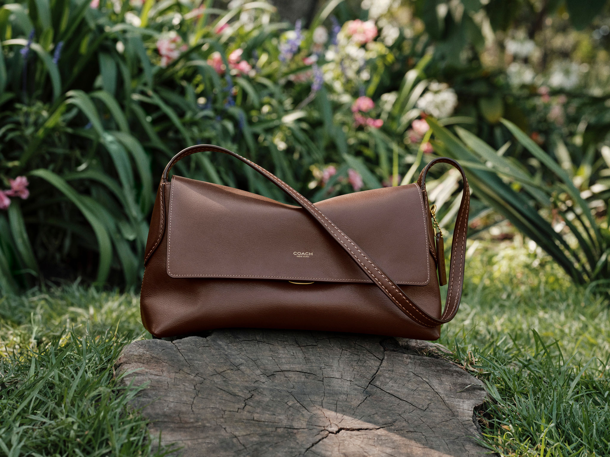 Brown Coach bag on a tree stump surrounded by flowers