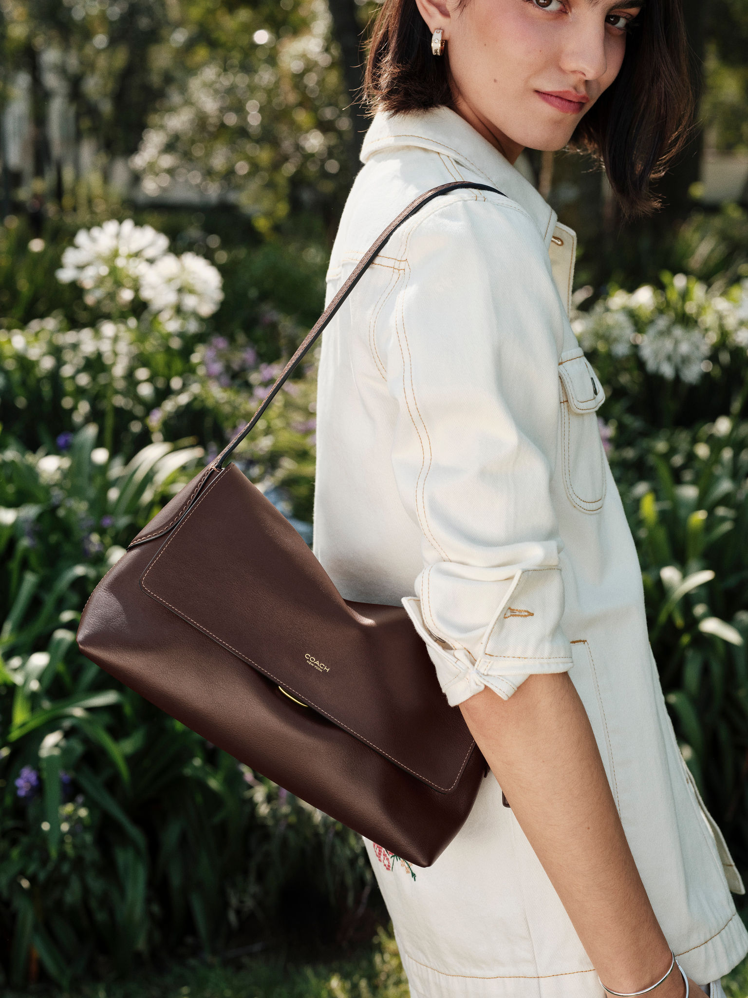 Model wearing a brown Coach bag in a garden