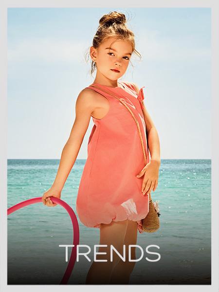 Girl in peach bubble dress holding a hoop at the beach. Shop the latest summer trends for kids.