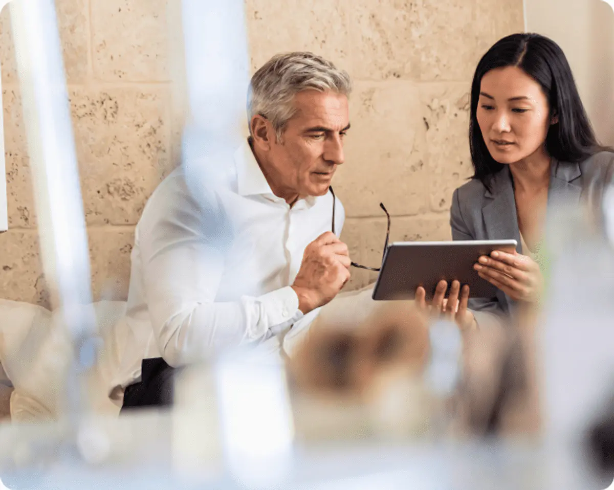 A senior executive and colleague reviewing a tablet together
