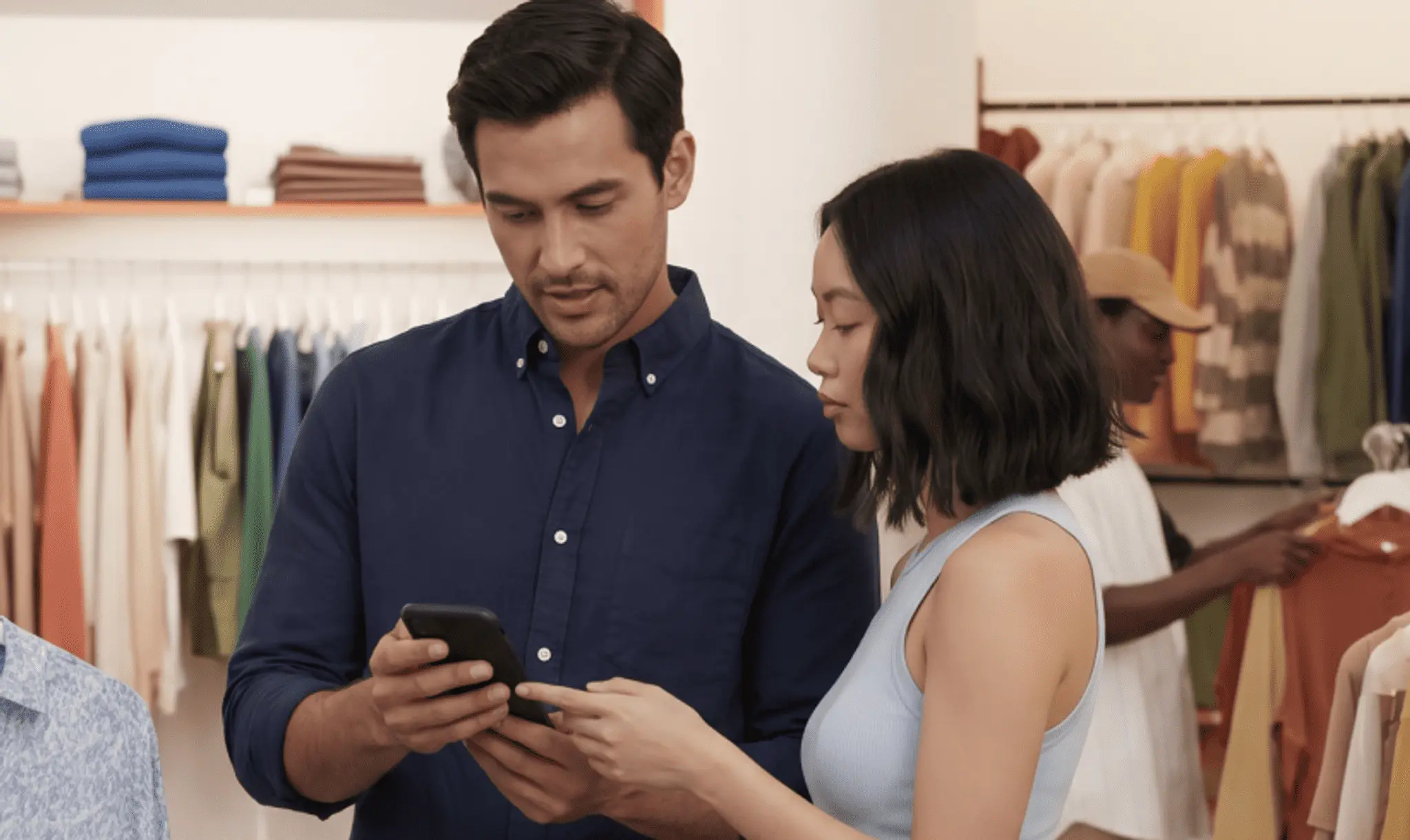 Store associate showing a customer a product on a smartphone in front of clothing racks
