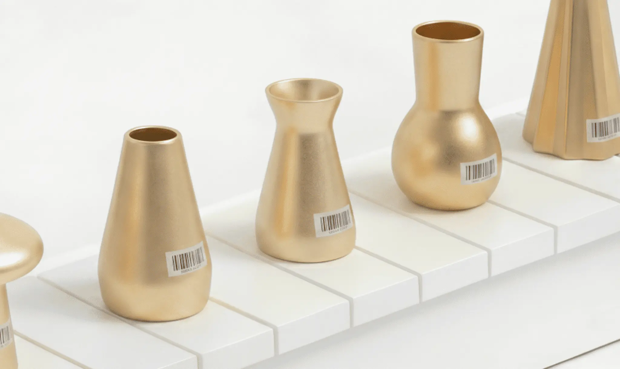 Gold vases on a shelf, each tagged with a barcode label for inventory tracking