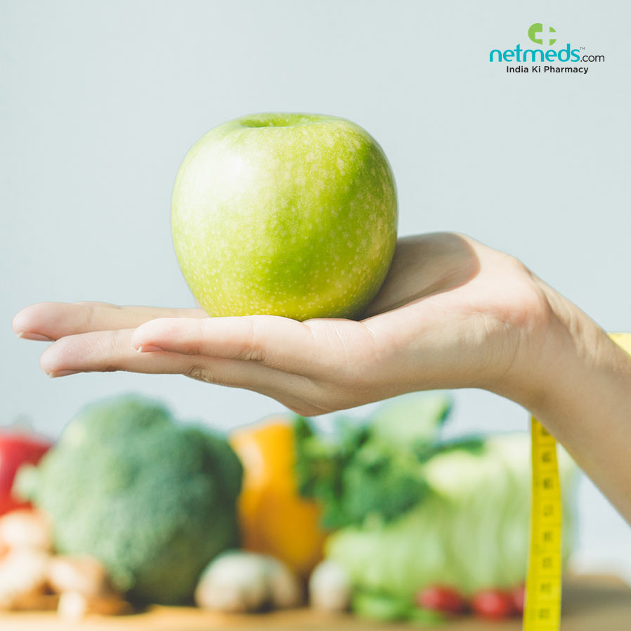 Vegetables in the background and holding the apple in one hand