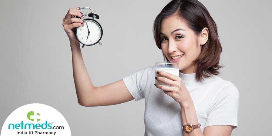 Girl with alarm in one hand drinking milk